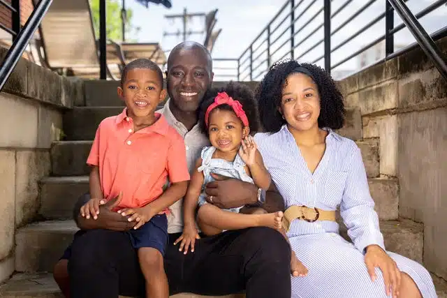 Family of four sitting together on outdoor concrete stairs, smiling at camera.